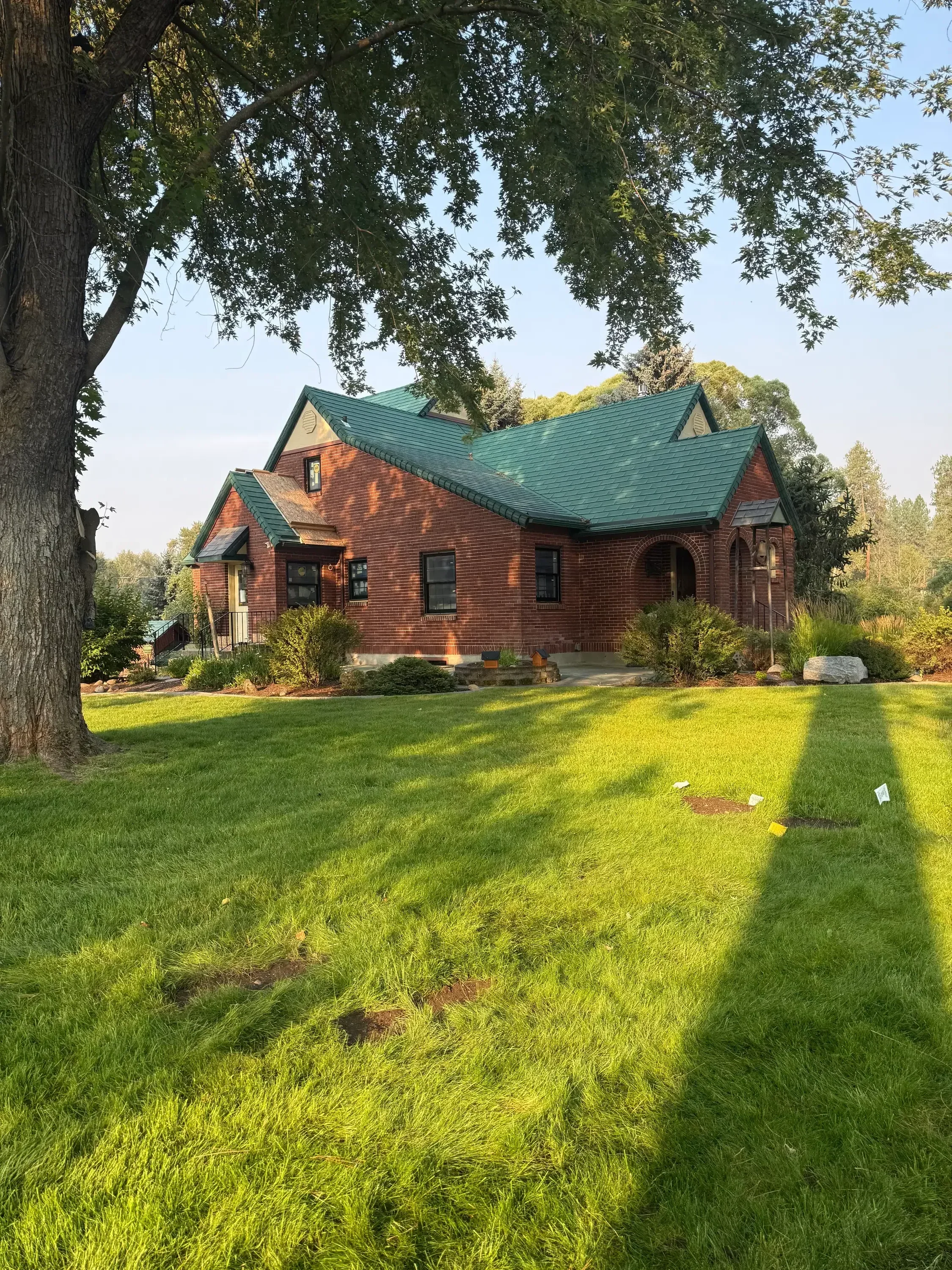 Brick home with turquoise metal roof and manicured lawn, surrounded by mature trees
