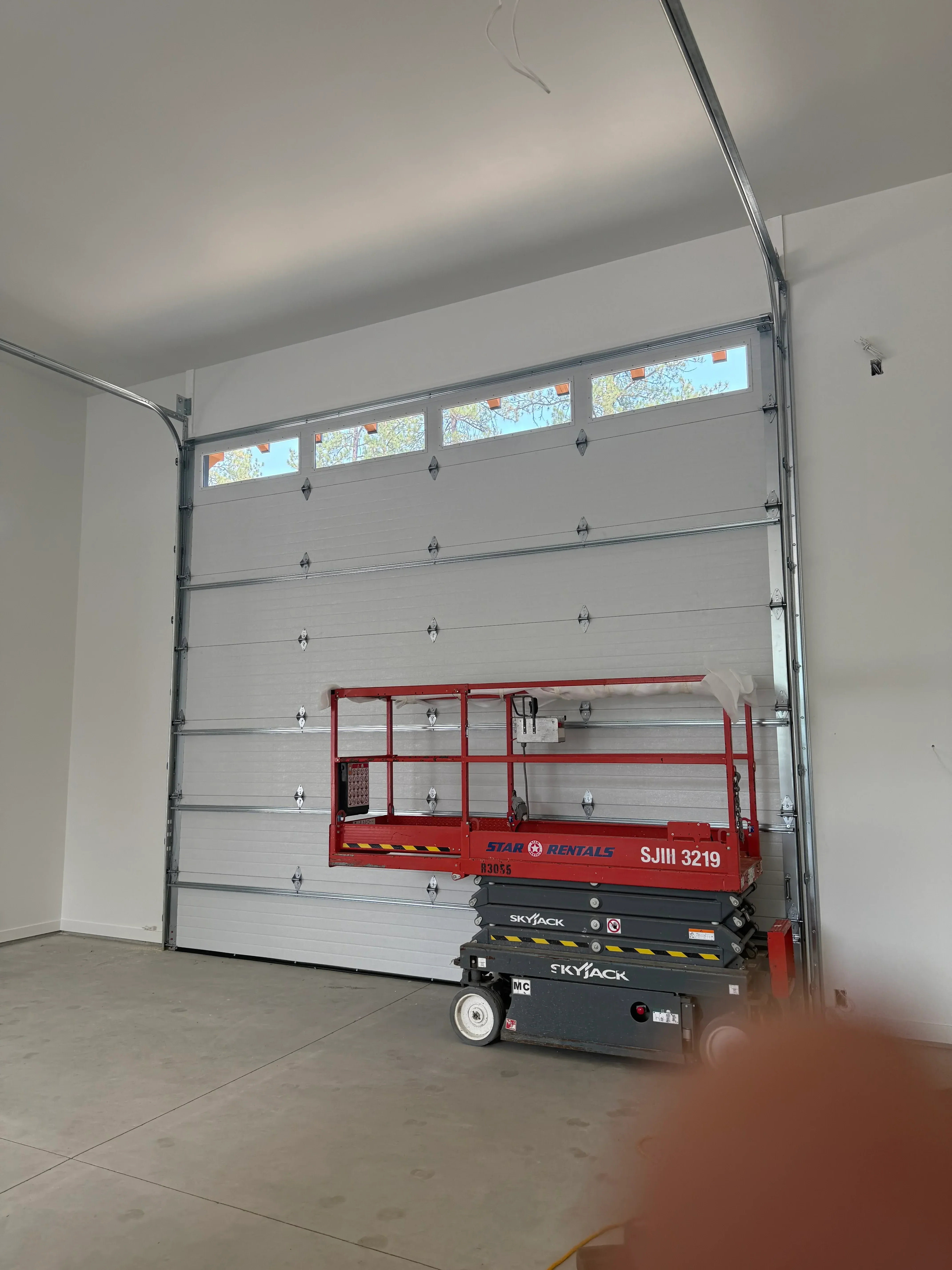 Installed garage door with aluminum frame, white panels, and red lift equipment during installation