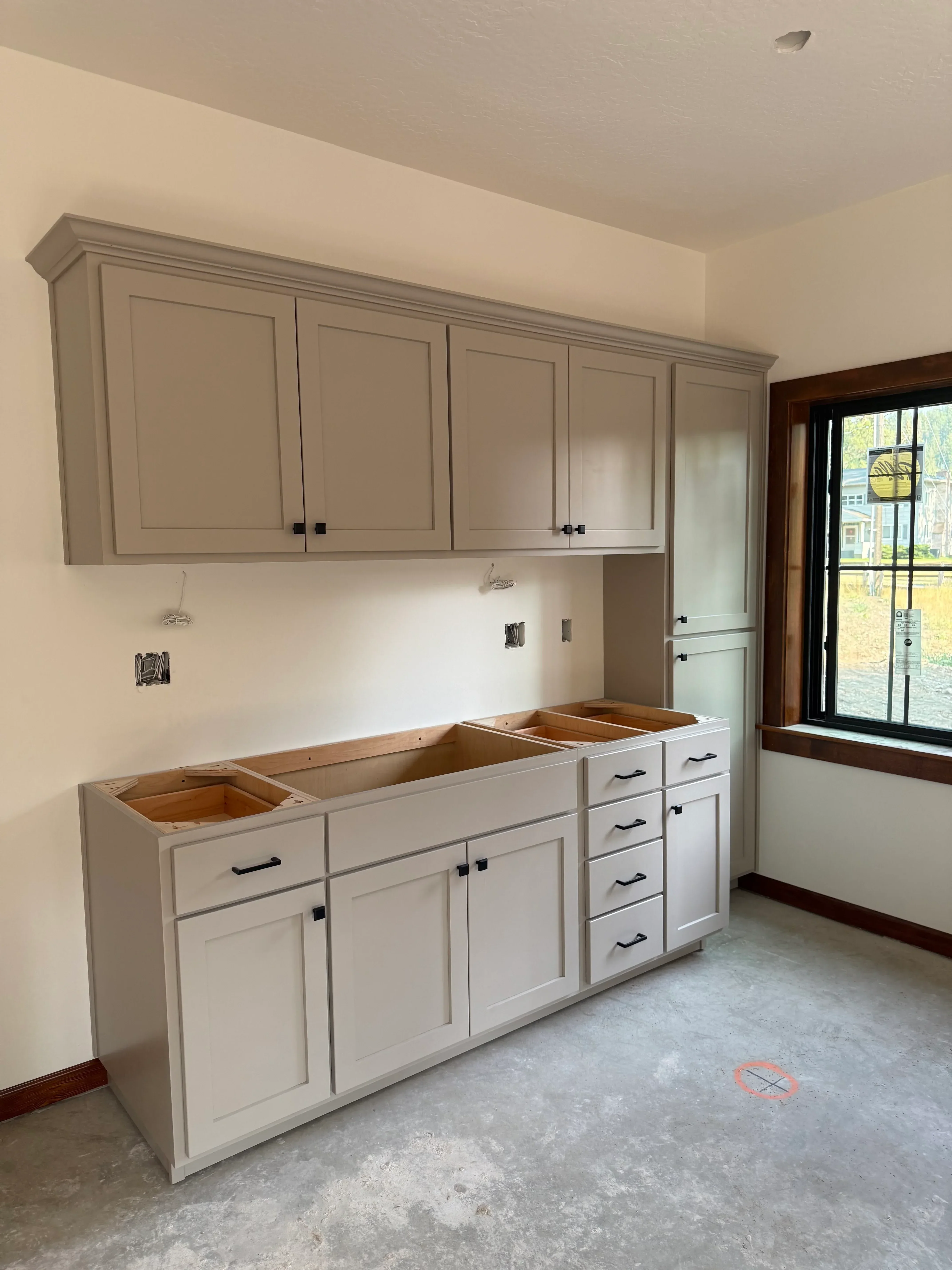 Installed white shaker-style kitchen cabinets with black hardware and electrical outlets