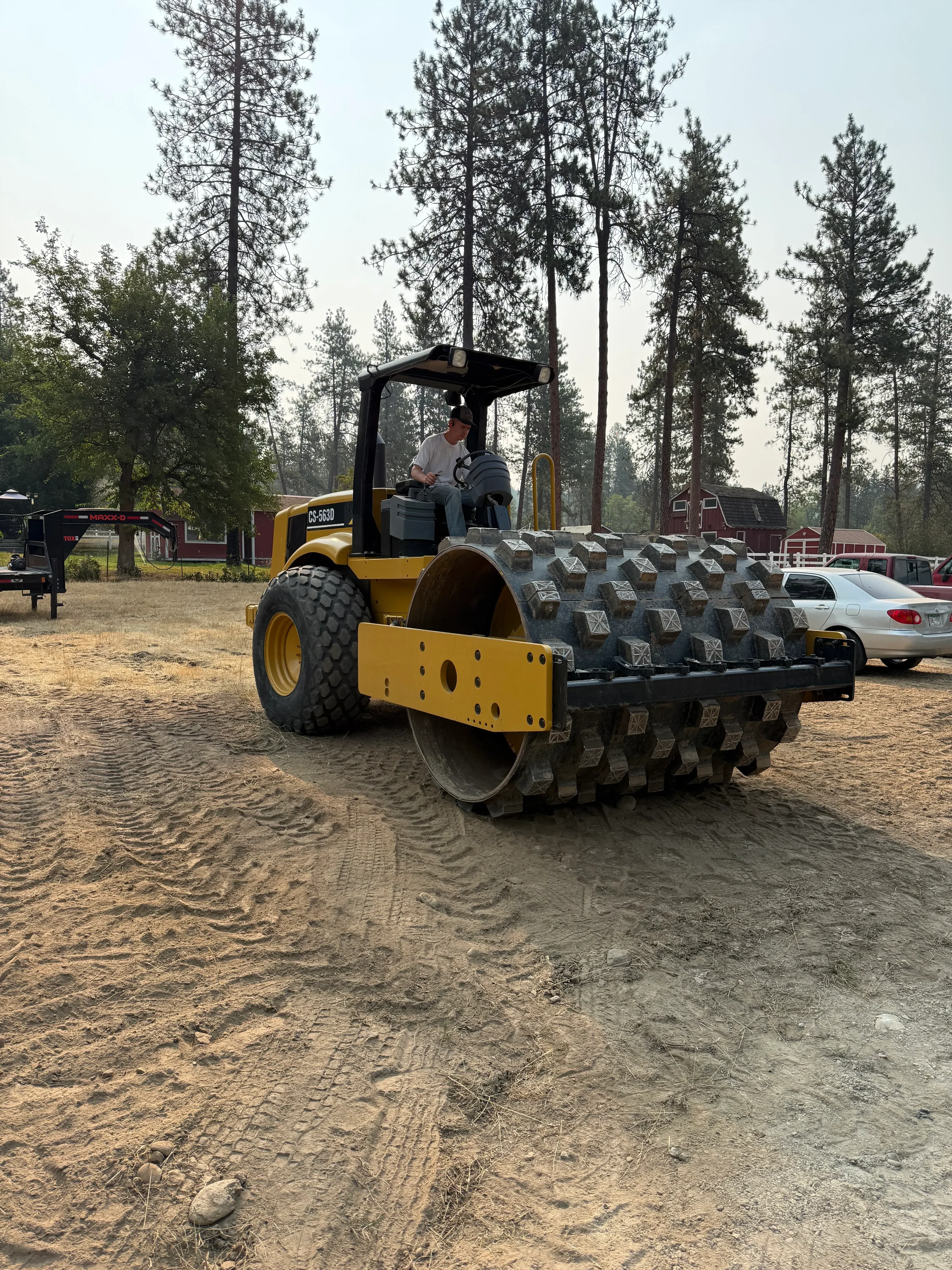 Yellow wheel loader grading unpaved driveway with compacted soil and residential structure in background